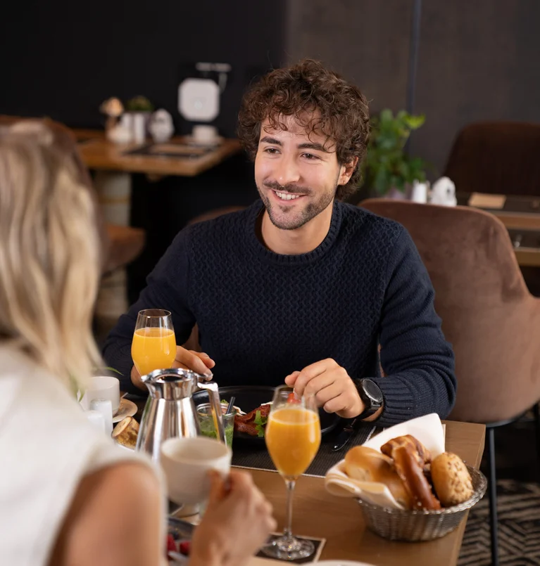 Die Adresse für Wellness in Bayern: Ihr Hotel in St. Englmar Junger Mann lächelt bei einem Frühstückstreffen im Café