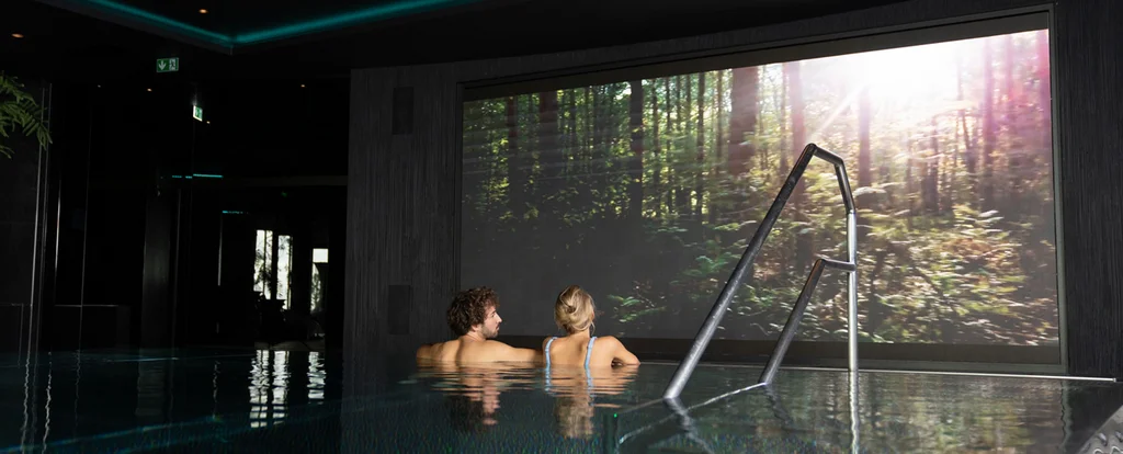 Die Adresse für Wellness in Bayern: Ihr Hotel in St. Englmar Paar entspannt im Innenpool mit großem Naturbild an der Wand
