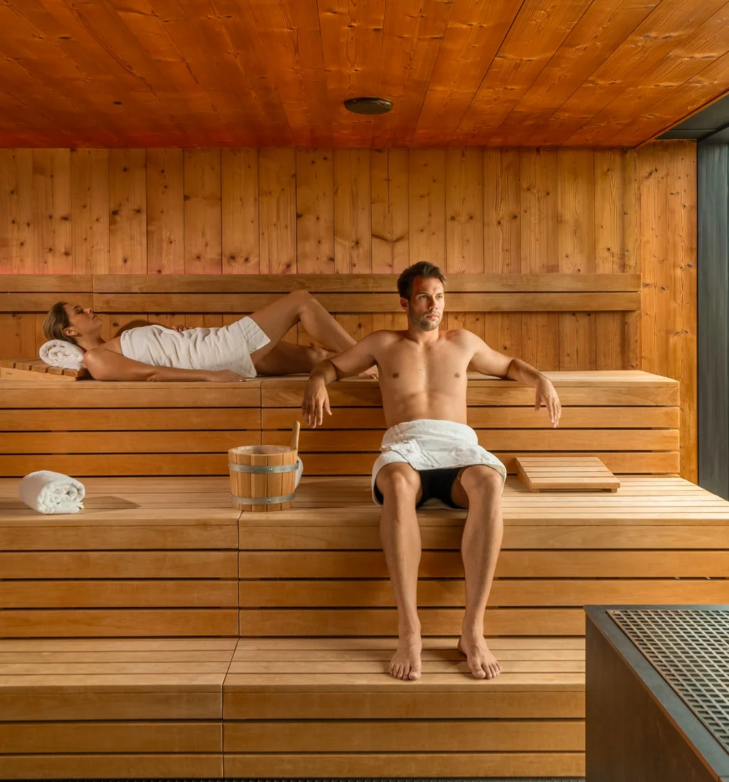 Die Adresse für Wellness in Bayern: Ihr Hotel in St. Englmar Mann und Frau entspannen in einer modernen Sauna mit Holzwänden und großen Fenstern