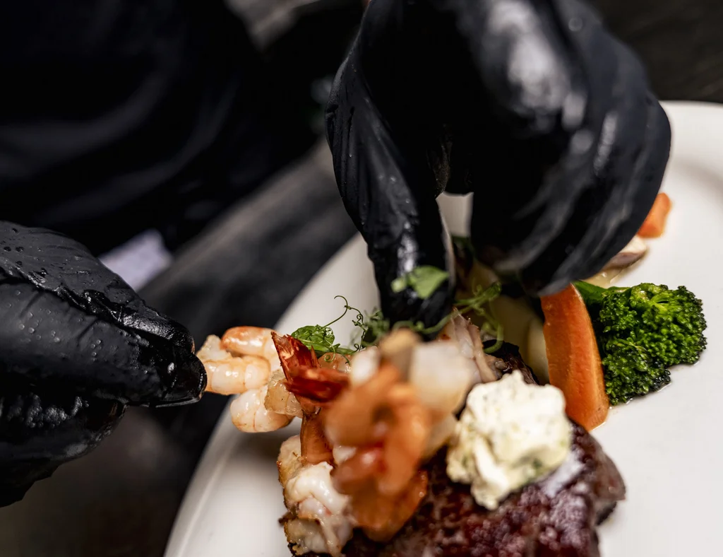Die Adresse für Wellness in Bayern: Ihr Hotel in St. Englmar Chef legt mit Handschuhen Garnele auf Steak mit Gemüse